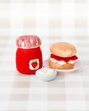 Red jar with a strawberry design and a toy burger on a checkered tablecloth.