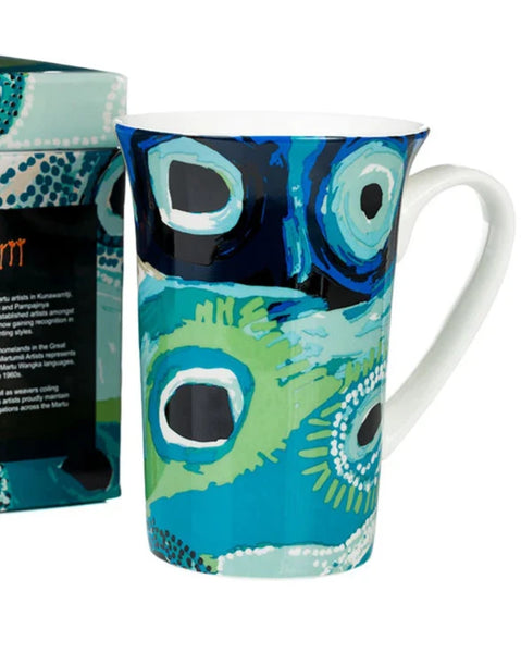 Colorful mug with peacock feather design next to its packaging on a white background